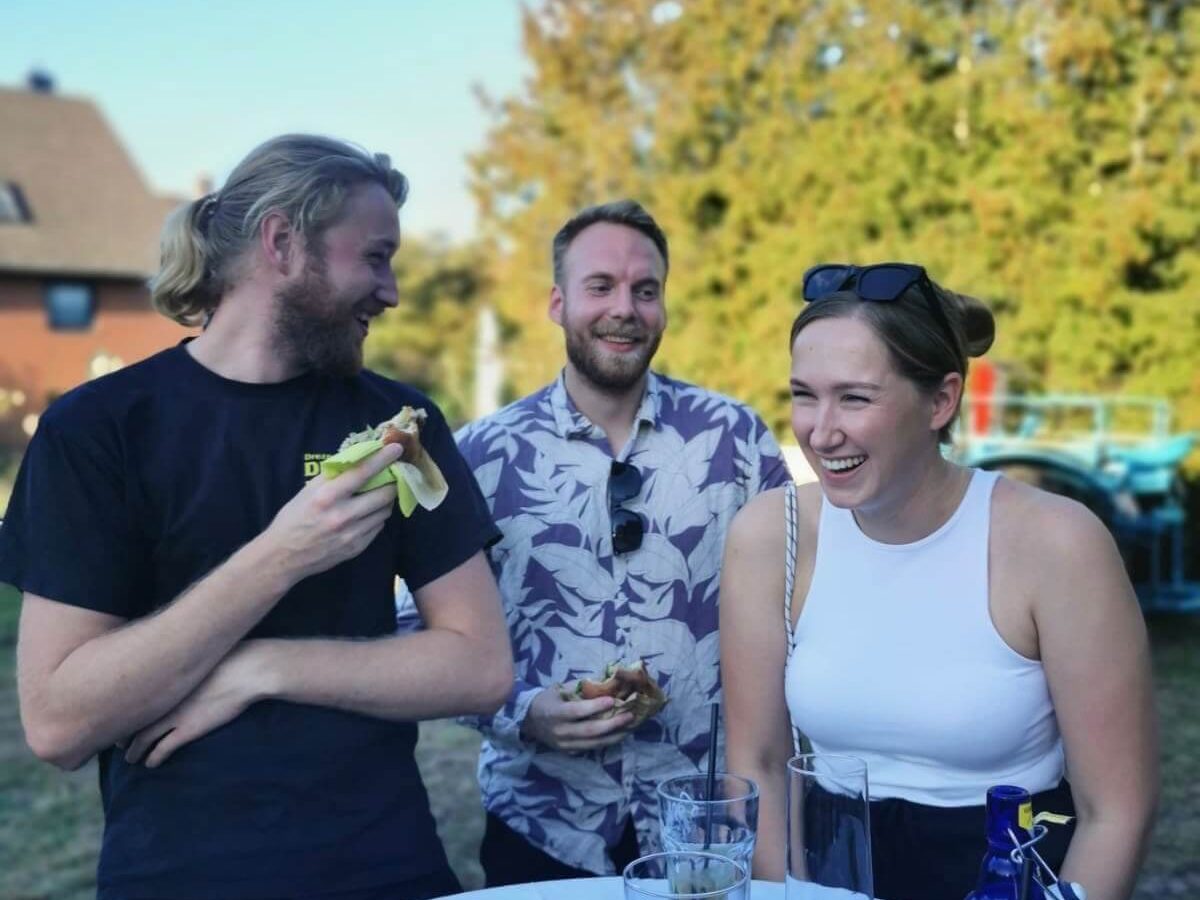 Drei Personen stehen beim Sommerfest zusammen und lachen.