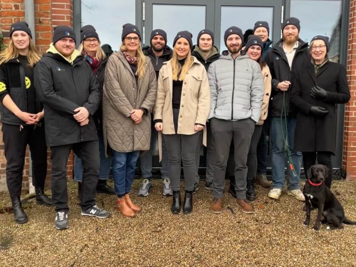 Mitarbeiter-Gruppenfoto vor dem Firmengebäude mit Strickmützen und Hund.