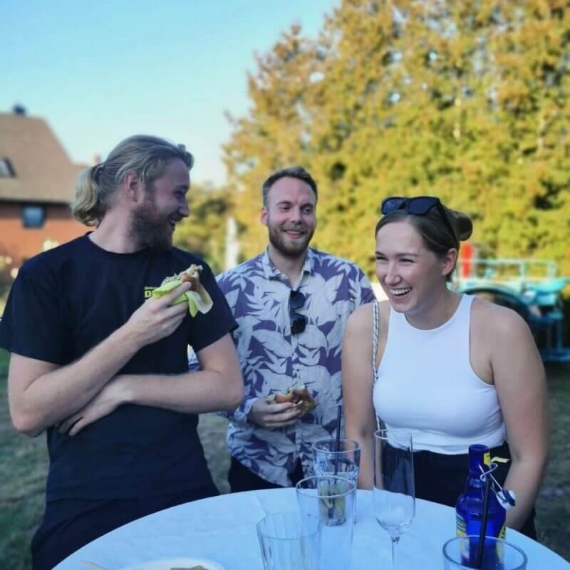 Drei Personen stehen beim Sommerfest zusammen und lachen.